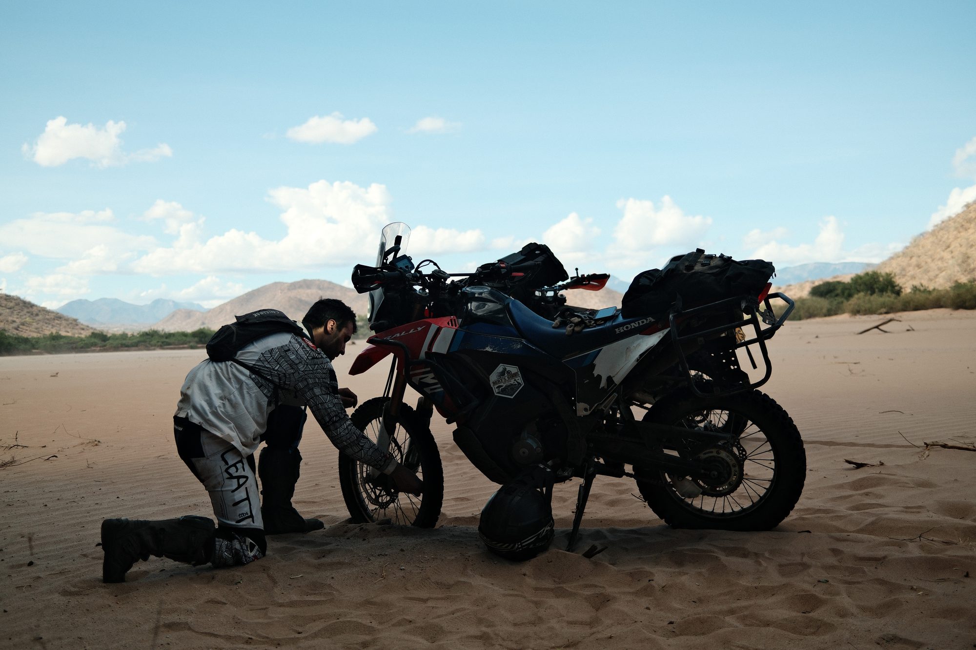 Riders working on a bike on the sand