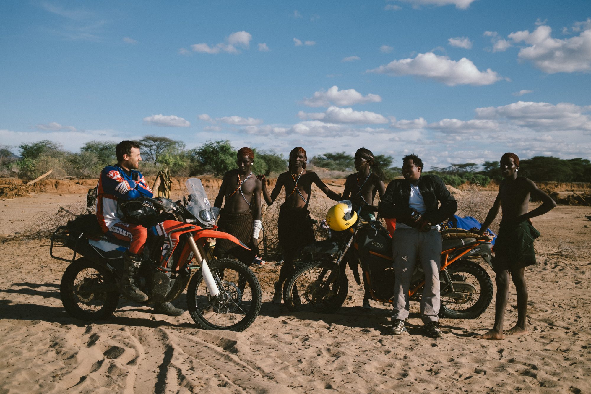 Riders and local people standing together with the bikes under a big sky