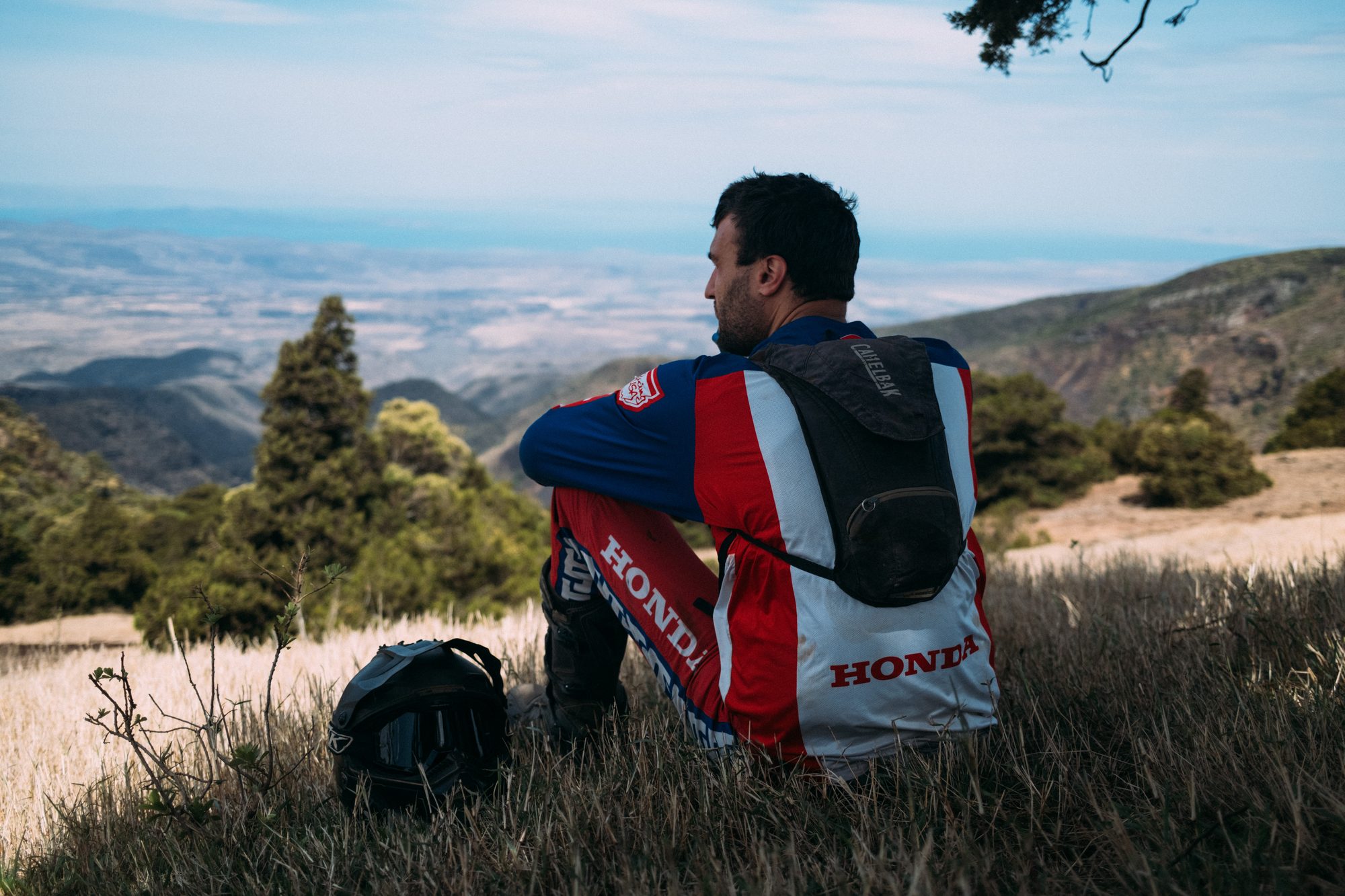 A rider in Honda kit sitting on a hillside looking out over the plains