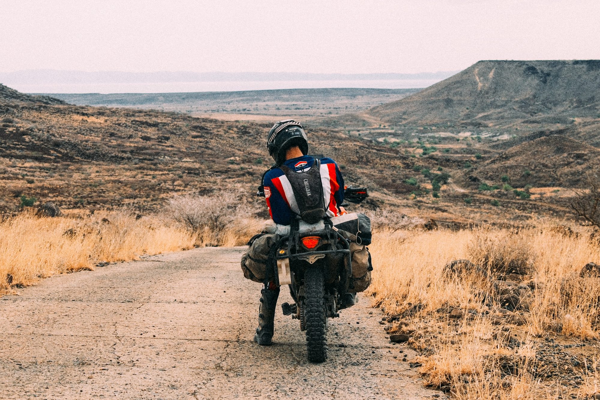 A rider on a laden motorbike looking down a road into a wide valley