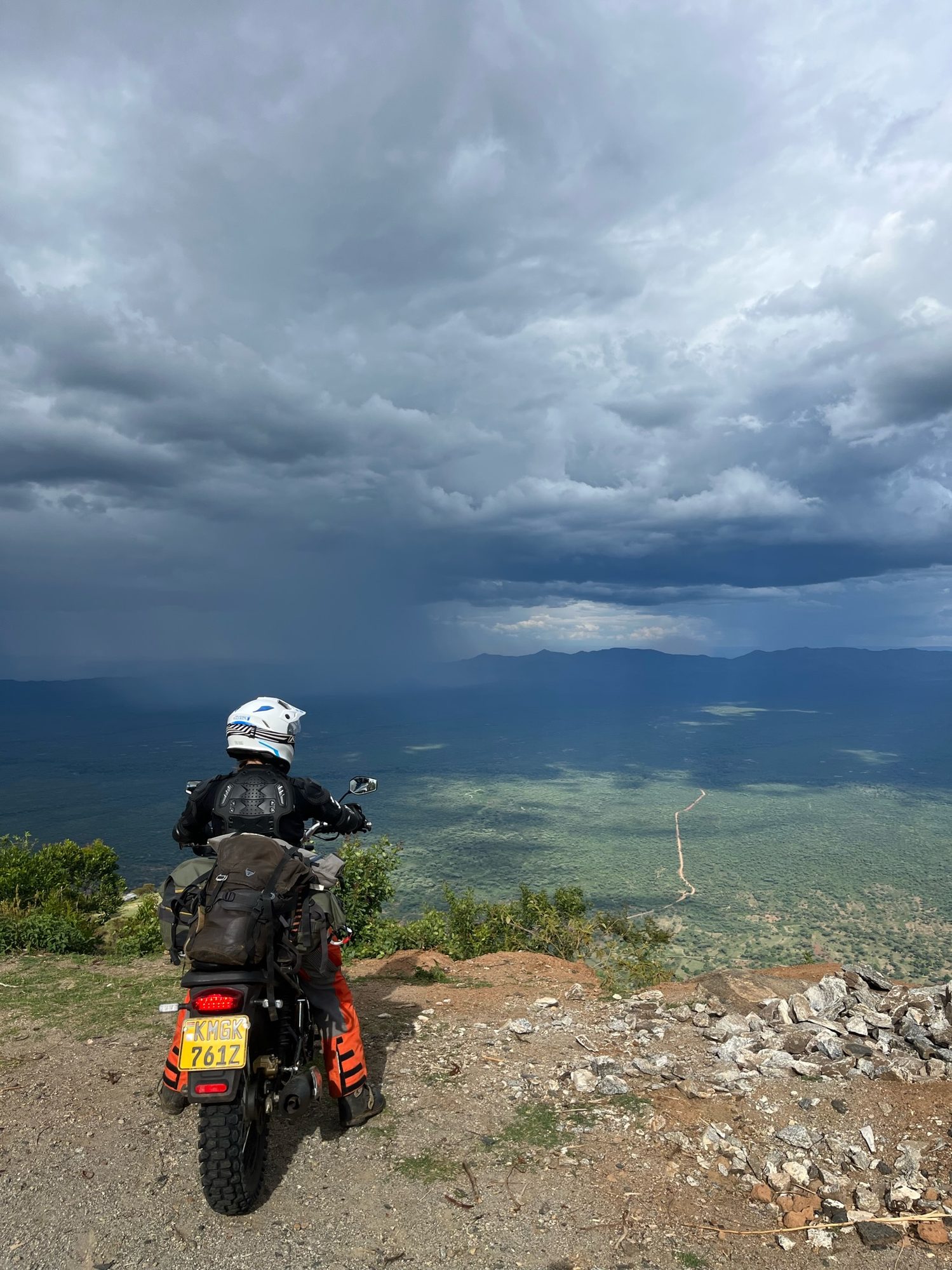 A rider pausing on a hillside under a storm sky, the valley below