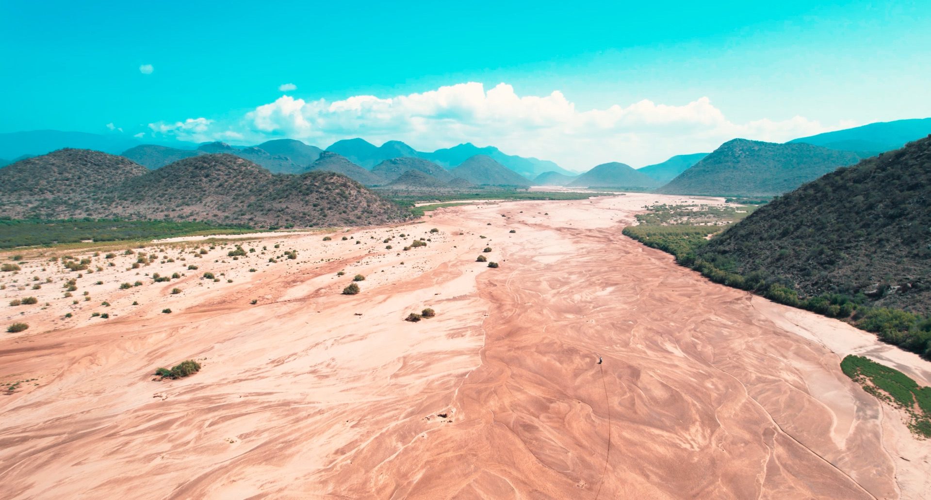 A wide dry riverbed, a lugga, running towards mountains under a big sky